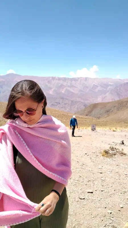 Andrea con anteojos de sol y un poncho rosa en un paisaje árido de montañas