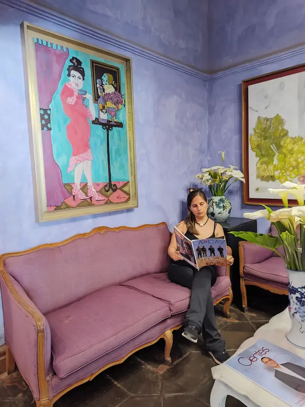 Andrea leyendo una revista sentada en un sillón violeta, bajo un cuadro colorido en una sala de paredes lilas