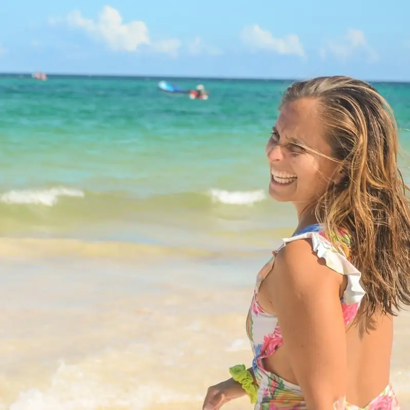 Andrea riendo con el pelo mojado en una playa de arena blanca y mar turquesa