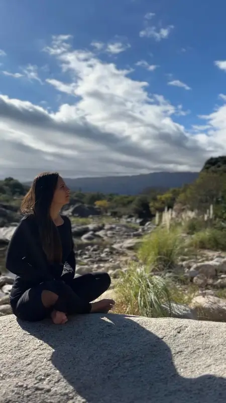 Andrea sentada sobre una gran roca mirando al cielo, junto a un río de montaña