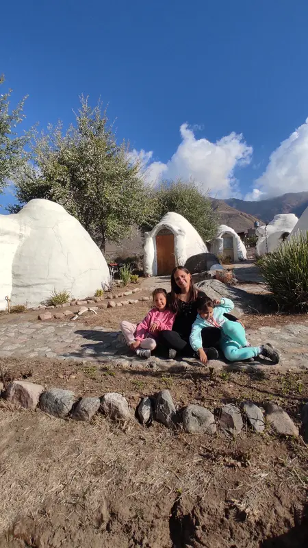 Andrea y sus mellizas sentadas en el piso de piedra entre casas domo blancas, con montañas y cielo azul de fondo