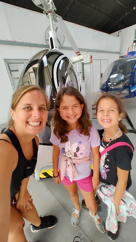 Andrea y sus dos mellizas sonriendo en una selfie dentro de un hangar, delante de un helicóptero