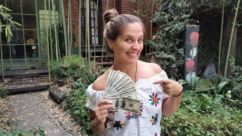 Andrea sonriente mostrando un abanico de billetes en un jardín, contenido sobre cuánto cuesta viajar