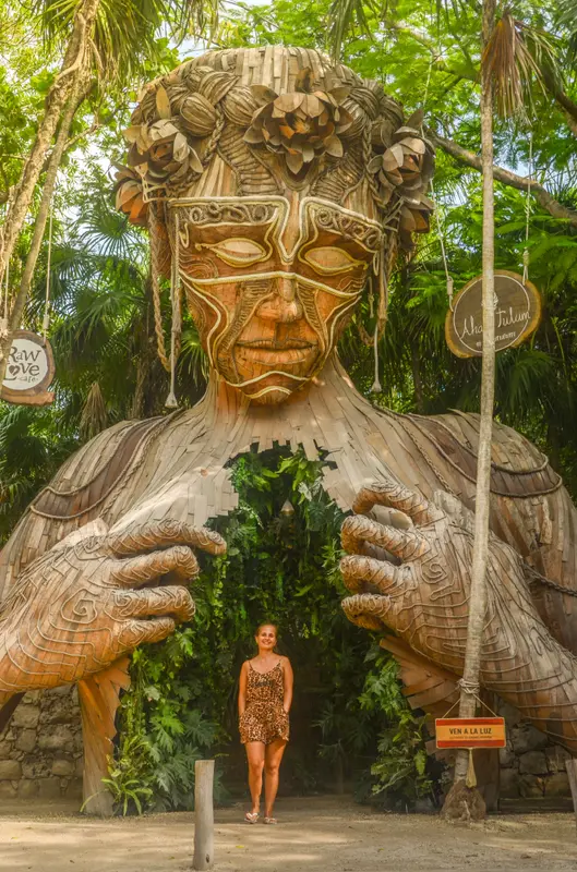 Andrea de pie en la entrada de una gran escultura de madera con forma de rostro, en medio de la selva