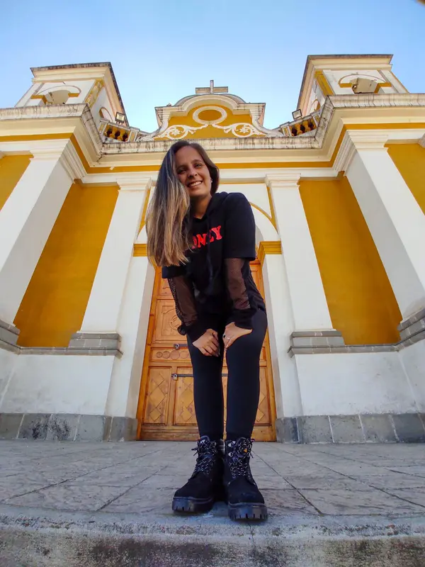 Andrea posando frente a la fachada amarilla y blanca de una iglesia colonial