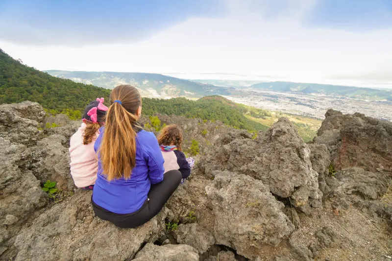 Andrea y sus mellizas de espaldas, sentadas sobre las rocas de un mirador frente a un valle entre montañas