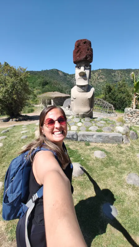 Andrea sonriendo en una selfie frente a una escultura de moai