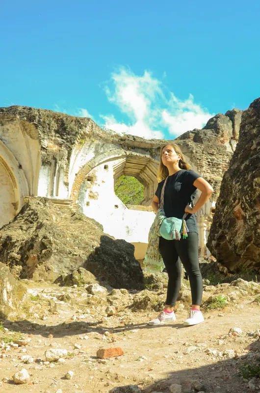 Andrea de pie entre ruinas de piedra con un arco abierto al cielo azul