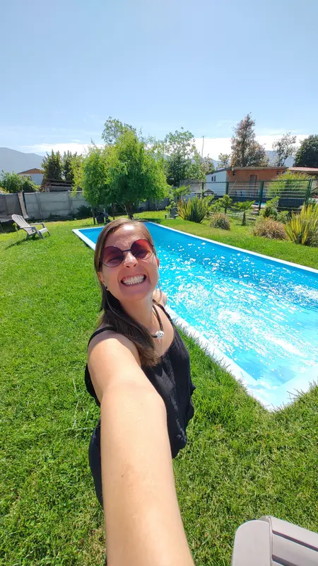 Andrea con anteojos de sol haciendo una selfie divertida en un jardín con césped, junto a una piscina